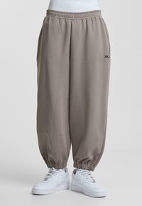 Lysegrå joggers med elastisk talje og manchetter, prydet med et lille logo foran. Båret med hvide sneakers.