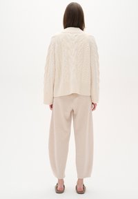 Maglione lavorato a maglia a coste color crema con orlo a coste, abbinato a morbidi pantaloni beige a sigaretta. L'outfit ha una silhoutte rilassata e una palette di colori neutri.