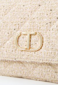 Teksturirana bež pletena torbica s šljokicama, koja ima zlatni metalni kopč s oznakom "TWINSSET" i zak quilted dizajn.