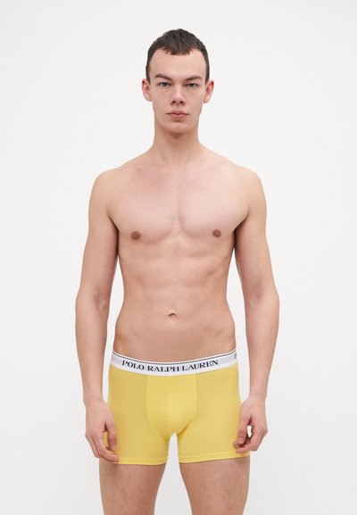 Sárga pamut boxer sort fehér derékkal, amelyen kék színnel van nyomtatva a "POLO RALPH LAUREN" felirat. A szabása testhez simuló, sima textúrával rendelkezik.