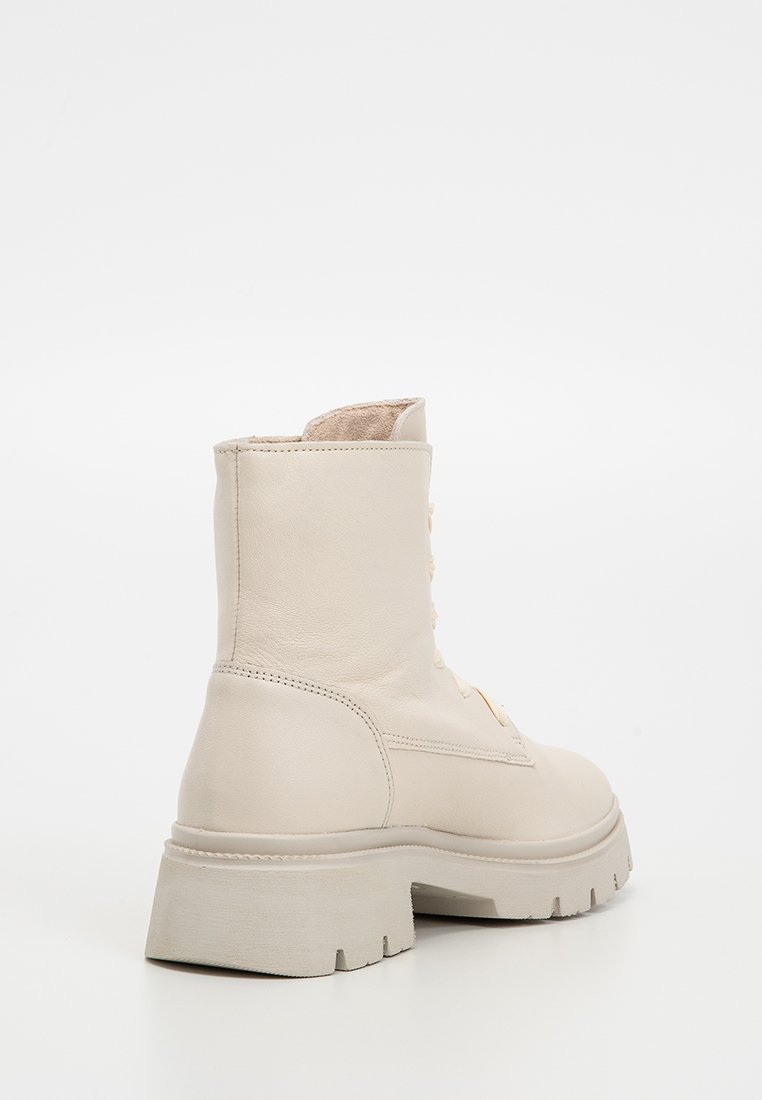 Beige Leder Stiefelette mit einer massiven Gummisohle, seitlichen Nahtdetails und Schnürung vorne. Glatte Textur, minimalistisches Design.