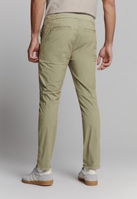 Heren licht olijfgroene broek met een slim fit, elastische tailleband en twee achterzakken, gecombineerd met grijze sneakers met witte strepen.