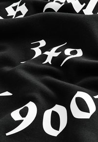 Tela negra con grandes y audaces números y letras en blanco. El material parece texturizado y suave, con pliegues y arrugas visibles.