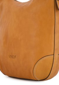Sac à bandoulière en cuir beige présentant une texture lisse, une forme courbée et des coutures contrastées. Logo "VENEZIA" embossé sur le côté.