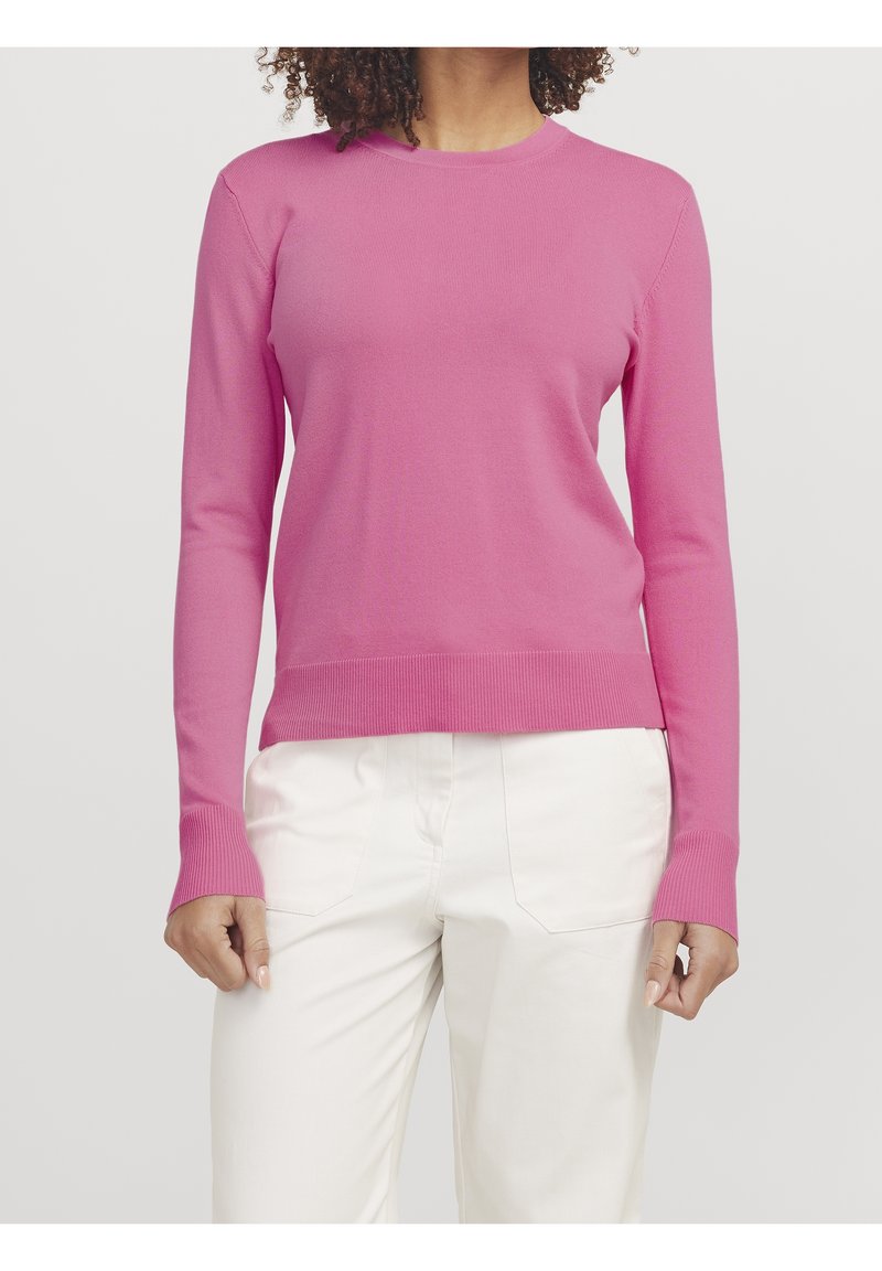 Pull en tricot rose à manches longues, avec poignets et ourlet côtelés. Texture douce, col rond, associé à un pantalon blanc.