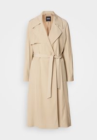 Trench-coat beige longueur genou avec larges revers, ceinture nouée à la taille, manches longues et détail pli sur l'épaule droite.