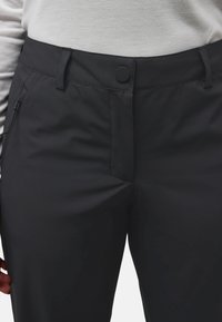 Nahaufnahme der Taille einer schwarzen Hose mit Knopfverschluss, Gürtelschlaufen, Reißverschluss, getragen mit einem hellgrauen Langarmshirt.