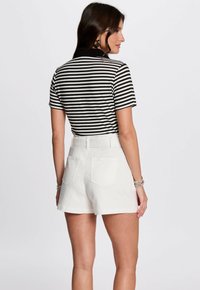 Zwart-witte gestreepte top met korte mouwen, gecombineerd met witte denim shorts. De shorts hebben achterzakken en een getailleerde pasvorm.