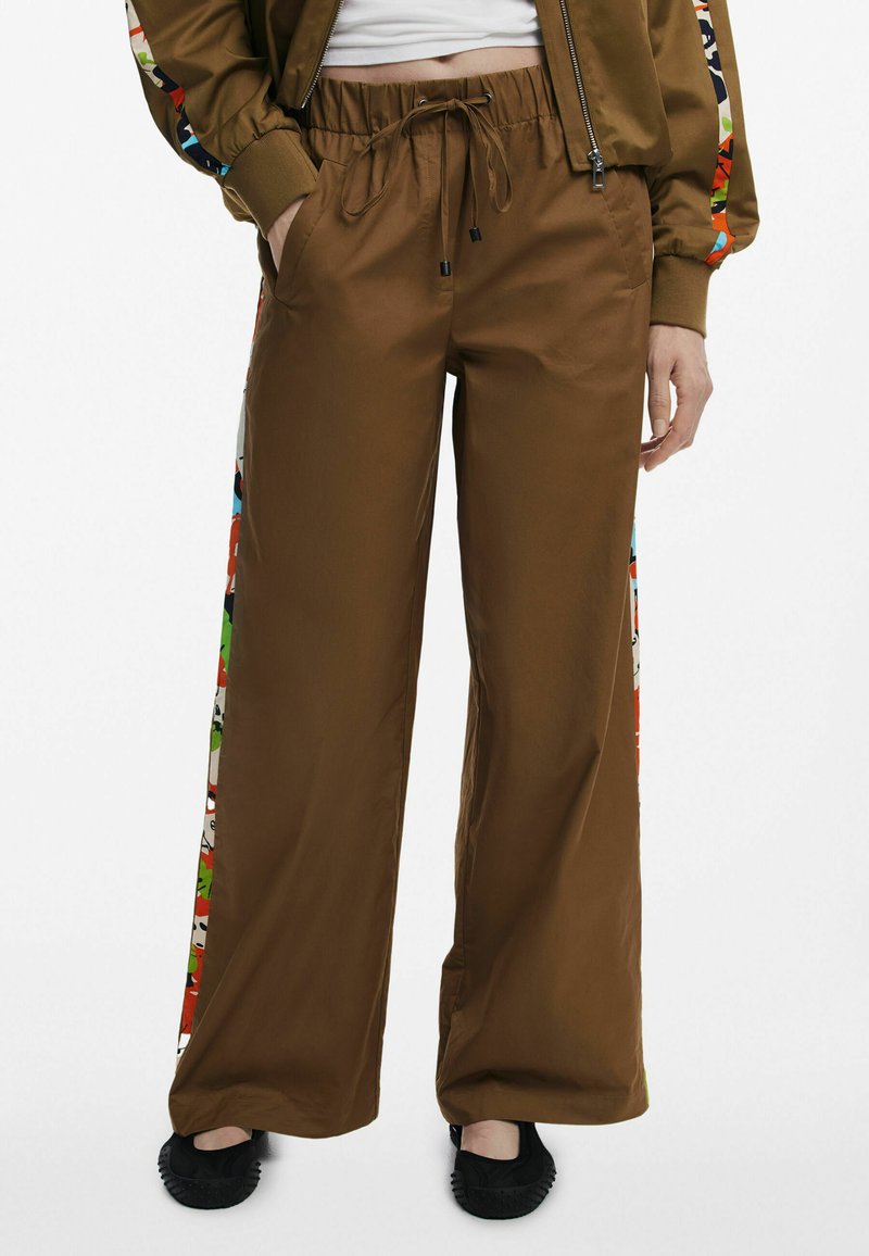 Hnedé široké nohavice s pásom na šnúrku, so farebnými vzorovanými bočnými panelmi. Vyrobené z hladkej látky, vhodné na každodenné nosenie.