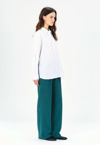 Camisa blanca de botón con mangas largas, combinada con pantalones anchos en un tono teal; tela lisa y suave con un diseño minimalista.
