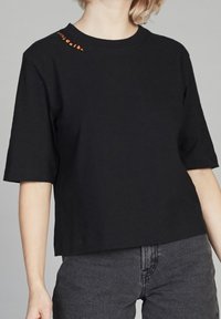 Camiseta de algodón negra de manga corta con un ajuste relajado, que presenta un pequeño logotipo naranja en el cuello del lado izquierdo.