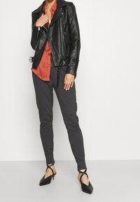 Svart läderbikerjacka med silverblixtlås, röd skjorta under, grå slim fit byxor och svarta spetsiga klackskor med korsade remmar.