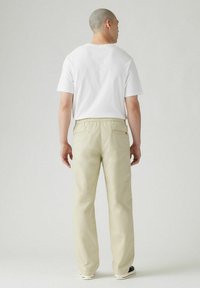 Beiga byxor med avslappnad passform, elastisk midja och två bakfickor. Matchade med en enkel vit t-shirt med rund hals.