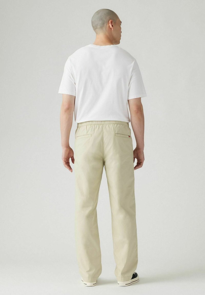 Pantalones beige con un ajuste relajado, cinturilla elástica y dos bolsillos traseros. Combinados con una camiseta básica blanca de cuello redondo.