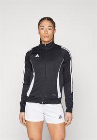 Black athletic jacket with white stripes, zippered front, high collar, and breathable fabric. Paired with white shorts featuring brand logo.
