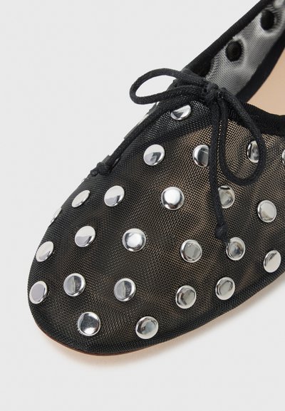 Ballet flats en mesh noir avec de grands clous argentés, un bout arrondi et un détail de noeud en dentelle noire sur le dessus. Doublure intérieure lisse.
