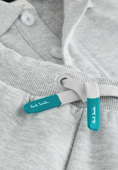 Pilkas sportinis megztinis su raišteliu, aksomo apykakle, skaidriais mygtukais ir raišteliu, turinčiu mėlynių akcentų bei "Paul Smith" prekės ženklu.