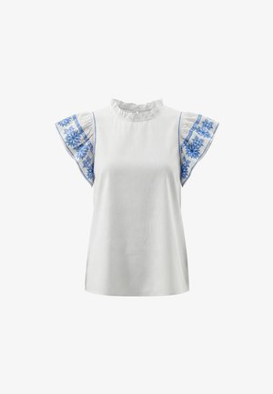 Hvid bluse med flæset halsudskæring og korte, flagrende ærmer med blå blomsterbroderi på en ensfarvet baggrund.