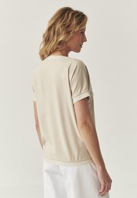 Camisa de manga corta beige con cuello redondo y un acento de rayas texturizadas en los puños y el dobladillo. Tejido suave, corte relajado.