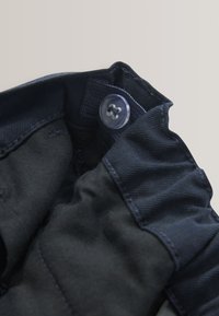 Gros plan sur une ceinture en tissu noir avec un bouton réglable et une section élastique pour un ajustement sécurisé.