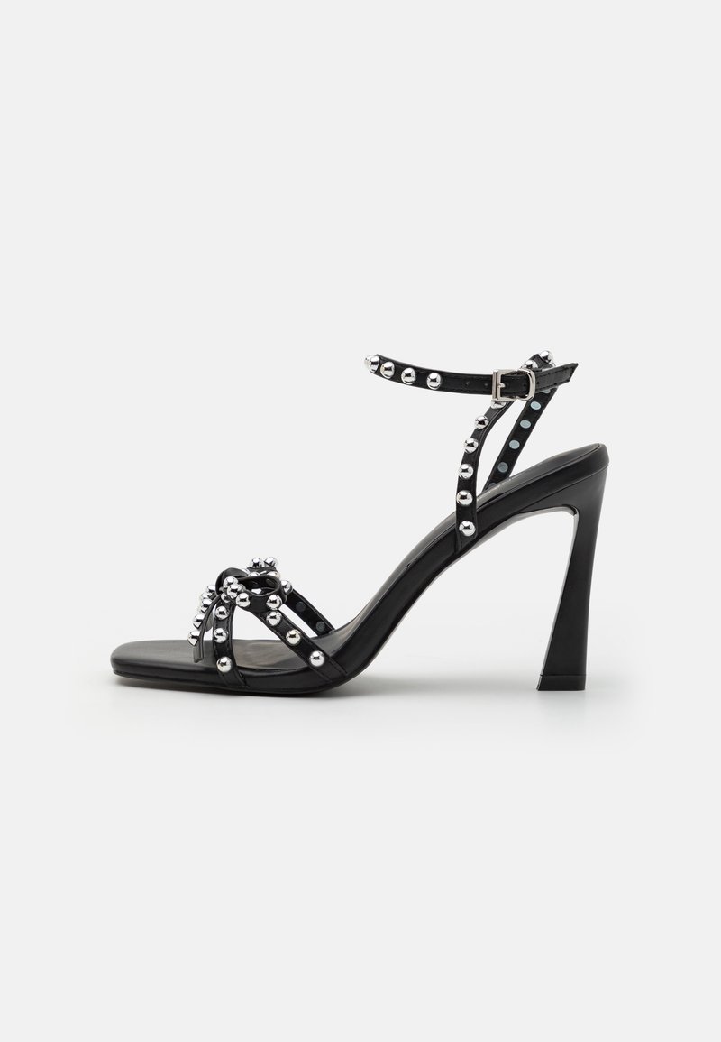 Svart høyhælte sandaler med bred stropp, naglede detaljer og et elegant design; har spenne-lukking og en glatt finish.