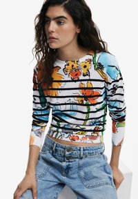 Mehrfarbiges Blumenmuster-Sweatshirt mit schwarzen Streifen, gerippter Textur und langen Ärmeln, kombiniert mit hochgeschnittenen hellblauen Denim-Jeans.