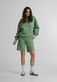 Roheline puuvillane üleraskustega sviiter ja lühikesed püksid, millel on soonikud. Sviitril on valge logo detail. Kanda valgeid sokke ja sneakers'e.