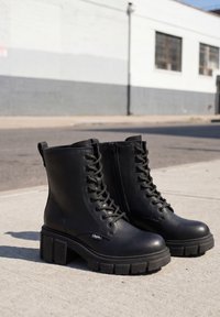 Pair of black leather lace-up combat boots with chunky soles placed on concrete sidewalk near street.