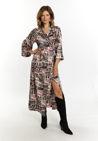 Rochie maxi în model abstract multicolor, cu talie legată, mâneci până la cot și fanta pe lateral, asortată cu cizme negre până la genunchi.