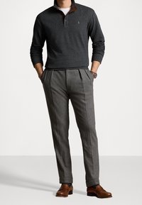 Dunkelgrauer Pullover mit braunem Kragen, kombiniert mit hellgrauen, gefalteten Hosen und braunen Slippern. Slim-Fit-Design mit strukturierter Oberfläche.