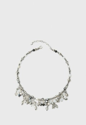 Collier avec chaîne en argent et petites perles et breloques suspendues dans des tons métalliques, noirs et transparents sur un fond clair.