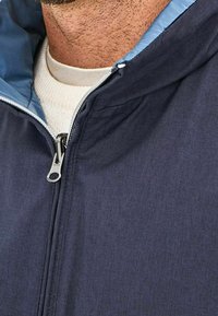 Veste à fermeture éclair bleu marine avec une doublure intérieure bleu clair, dotée d'une fermeture éclair argentée et d'un tissu texturé, conçue pour le confort et la chaleur.