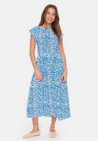 Blå mittlång klänning med vitt, abstrakt leopardtryck, featuring korta volangärmar och en smockad bodice. Bärs med beiga vävda ballerinas.