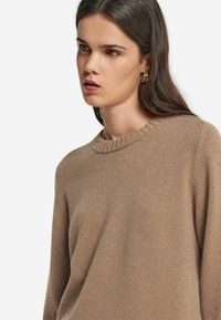 Brązowy sweter z dzianiny z ribbowanym okrągłym dekoltem. Materiał ma miękką teksturę i luźny krój, posiada długie rękawy.