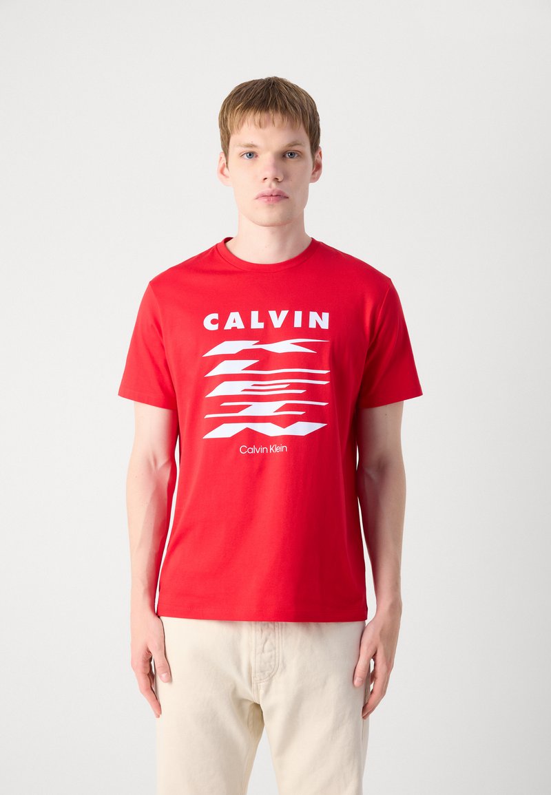 T-shirt en coton rouge avec un logo blanc et un design graphique sur le devant. Manches courtes, col rond, texture lisse et coupe régulière.