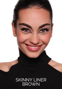 Brązowy cienki eyeliner na modelce o ciemnych włosach, ubranej w czarny golf. Jasne tło podkreśla eyeliner.