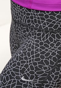Leggings negros con un patrón geométrico gris, con una cinturilla elástica y un pequeño logo blanco de Nike. Tejido suave y elástico.