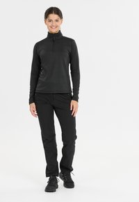 Zwarte langarmpullover met een halve rits, in combinatie met zwarte broeken en zwarte wandelschoenen; gladde textuur en een aangesloten ontwerp.