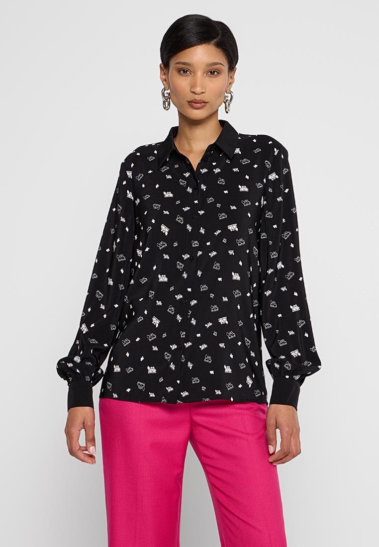 Camisa negra de manga larga con un patrón disperso en blanco y verde, cuello abotonado y mangas con puños, combinada con pantalones rosas.