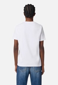 White cotton t-shirt with short sleeves, round neckline, and straight cut. Worn with blue denim jeans, showing minimalistic design and texture.