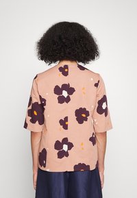Top de manga curta em tecido rosa suave, com um padrão floral em tons de roxo escuro e laranja, finalizado com um detalhe de costura nas costas.