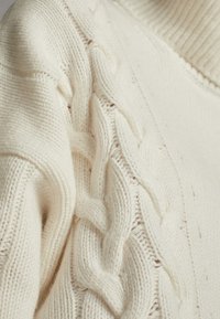 Kremowy sweter w splot warkoczowy z teksturowanymi wzorami i ribbowanym kołnierzem, wykonany z miękkiej, grubej przędzy dla ciepła i komfortu.