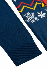 Sezione di un maglione lavorato a maglia blu navy con motivi a fiocco di neve bianchi, zigzag rossi e gialli brillanti e polsini a coste.