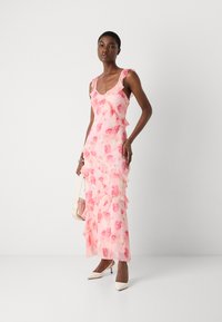 Pink floral dress with ruffled hem, made of lightweight fabric. Features a scoop neckline and spaghetti straps. Paired with beige heels and a pink bag.