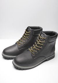 Paire de bottines noires en cuir Fila avec col rembourré, lacets jaunes et noirs, et semelles en caoutchouc gris sur fond blanc.
