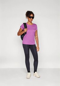 Lila atletisk t-shirt med korta ärmar, svarta leggings med strukturerade detaljer och vita sneakers. Bärs med solglasögon och en svart ryggsäck.