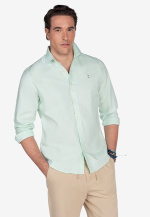 Camisa de botonadura en verde menta con un corte relajado, mangas largas enrolladas en los puños y un pequeño acento bordado en el pecho.