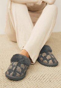 Gray slippers with bear patterns, featuring a plush gray fur lining and a rubber sole. The fabric has a smooth texture and soft feel.