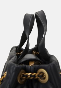 Sac à main noir avec une texture en matelassé. Doté de quincaillerie dorée, d'un détail en chaîne et de deux poignées robustes. La fermeture est de type cordon.