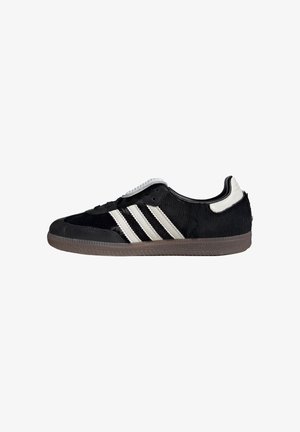 Zwarte lage sneaker met witte strepen, witte hieltab en grijze, gestructureerde zool, zijaanzicht op een witte achtergrond.